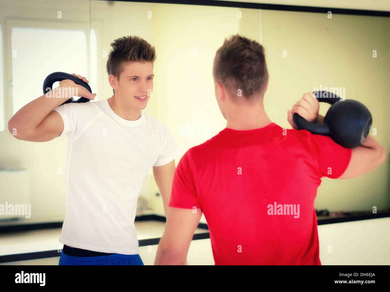 Due prestanti giovani in palestra esercizio con kettlebells, sorridente Foto Stock