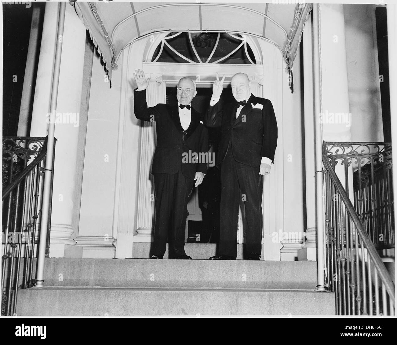Questa fotografia storica cattura Winston Churchill che mostra il suo cartello "V for Victory", mentre il presidente Harry S. Truman ondeggia fuori Blair House, un simbolo della cooperazione internazionale e della leadership in tempo di guerra durante la seconda guerra mondiale Foto Stock