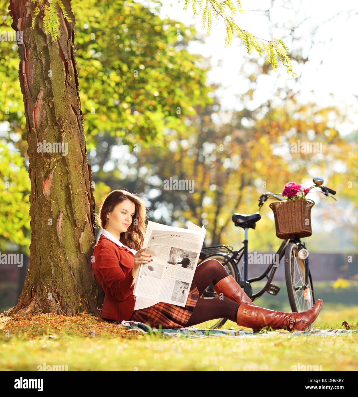 Giovane donna con la bicicletta seduti su un prato verde e la lettura di un quotidiano in un parco Foto Stock