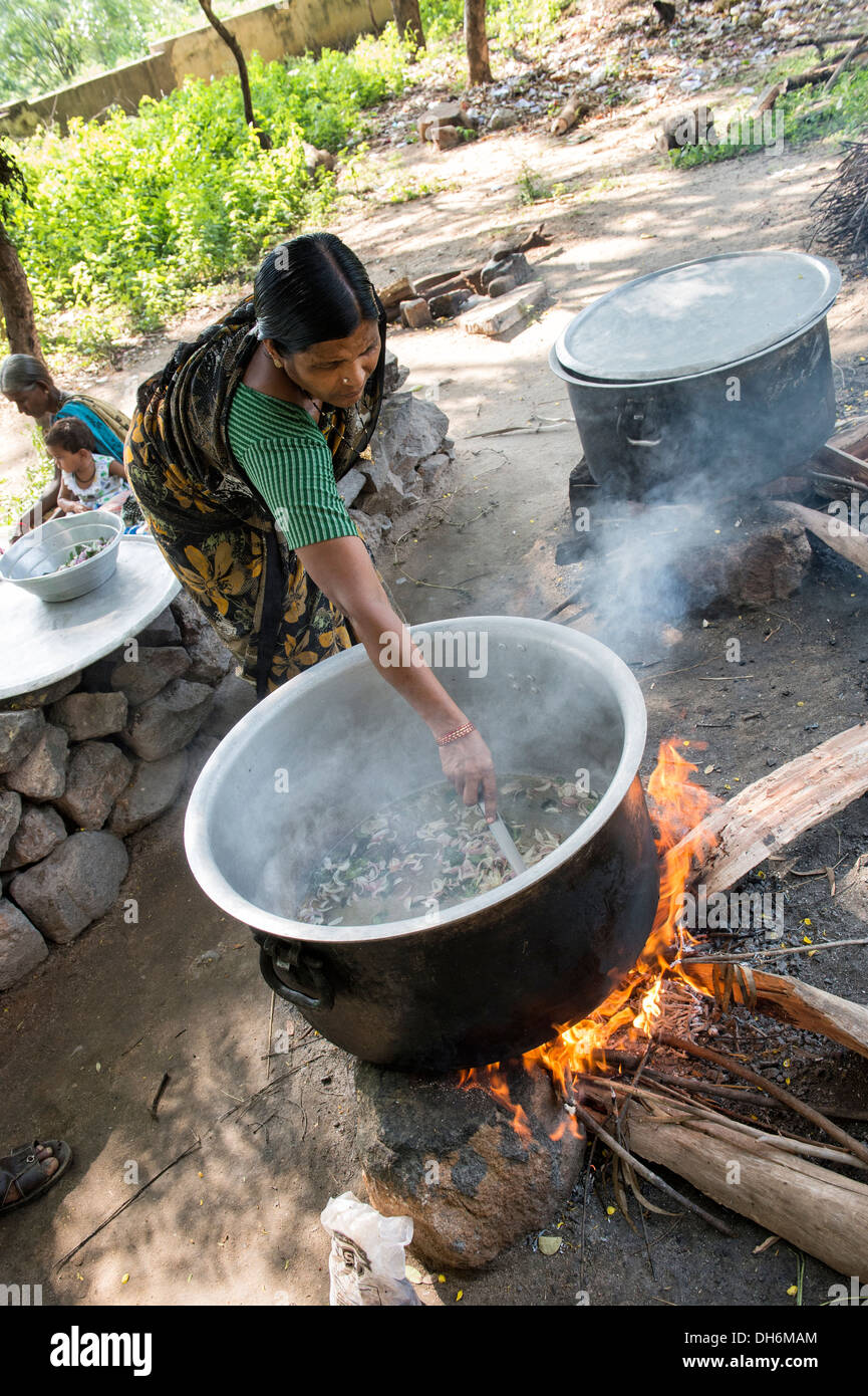 Donna indiana cucinare i pasti scolastici su fuochi aperti in corrispondenza di una zona rurale villaggio indiano di alta scuola. Andhra Pradesh, India Foto Stock