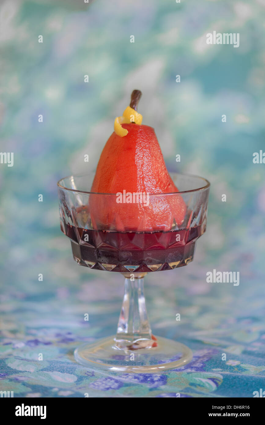Pera affogata nel vino rosso su sfondo colorato in un bicchiere che serve il pezzo. Foto Stock