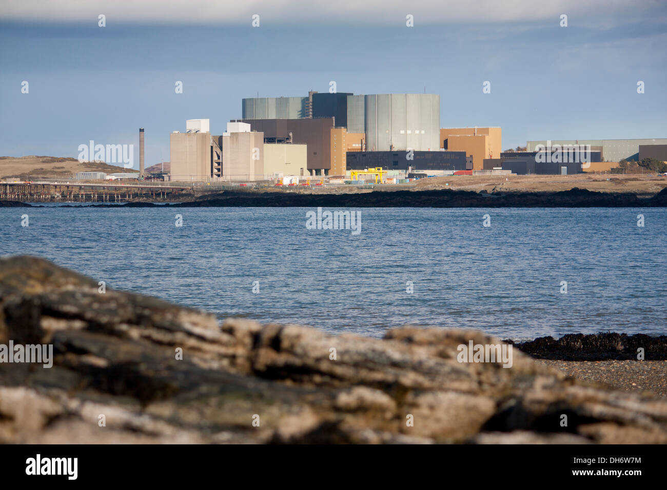 Wylfa Centrale Nucleare visto da Cemlyn Bay con le rocce in primo piano Anglesey North Wales UK Foto Stock
