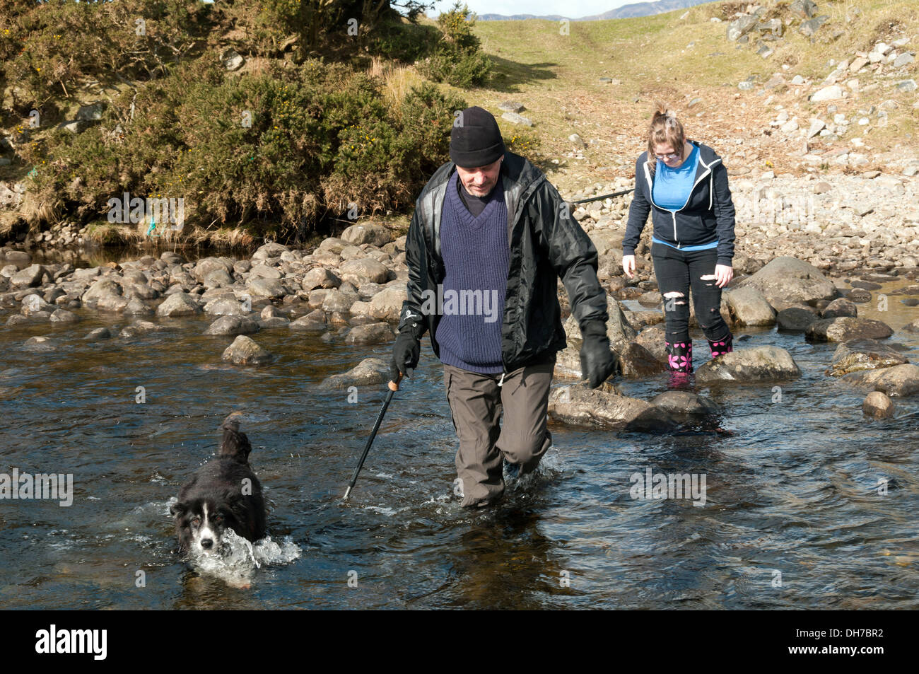 Due escursionisti e un cane guadare il Abhainn Inbhir Guiserein river a Inverguseran, Knoydart, regione delle Highlands, Scotland, Regno Unito Foto Stock