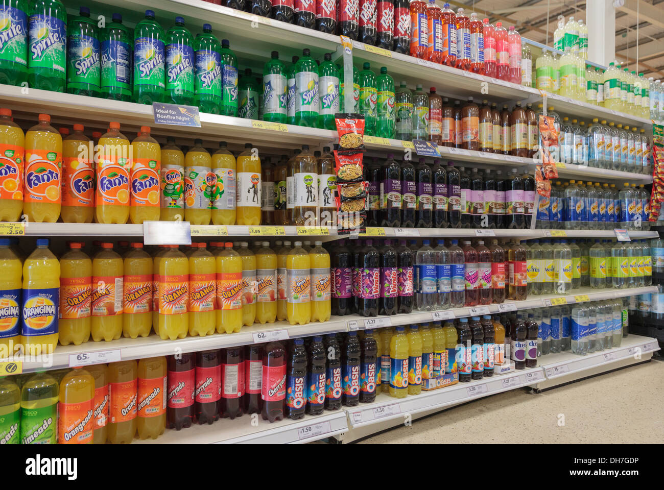 Una varietà di bottiglie di frizzanti bevande zuccherate per la vendita in un supermercato Tesco ripiani del corridoio. Regno Unito, Gran Bretagna Foto Stock