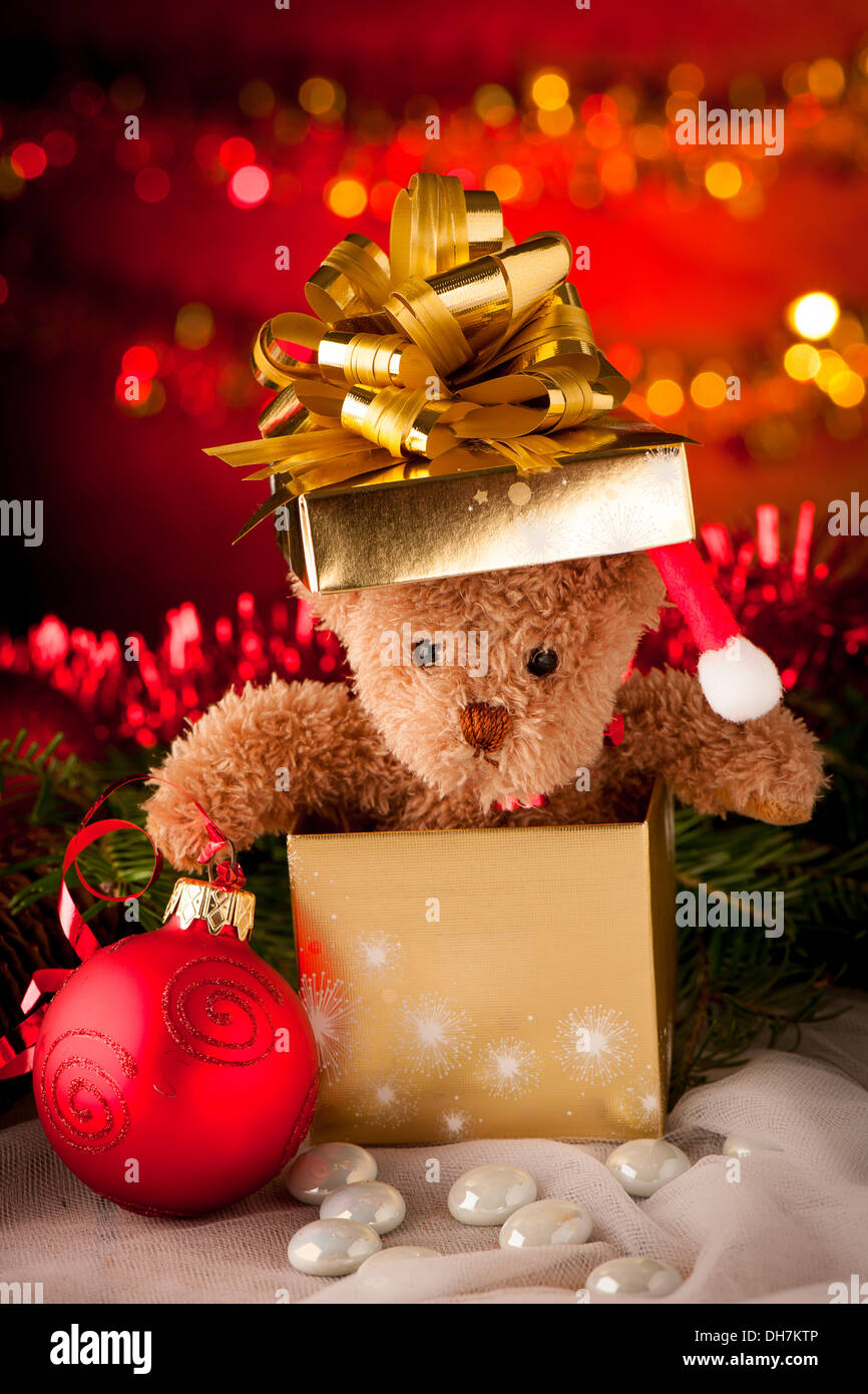 Orso di peluche in golden presente casella Ornamenti natale con luci in background e sfera rossa Foto Stock