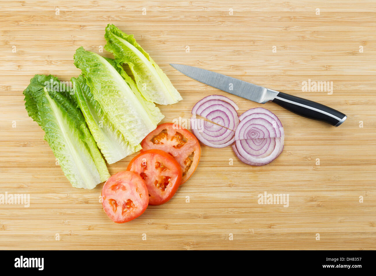 Foto orizzontale di taglio fresco lattuga, cipolla e le fette di pomodoro su di bamboo naturale scheda con coltello da cucina Foto Stock