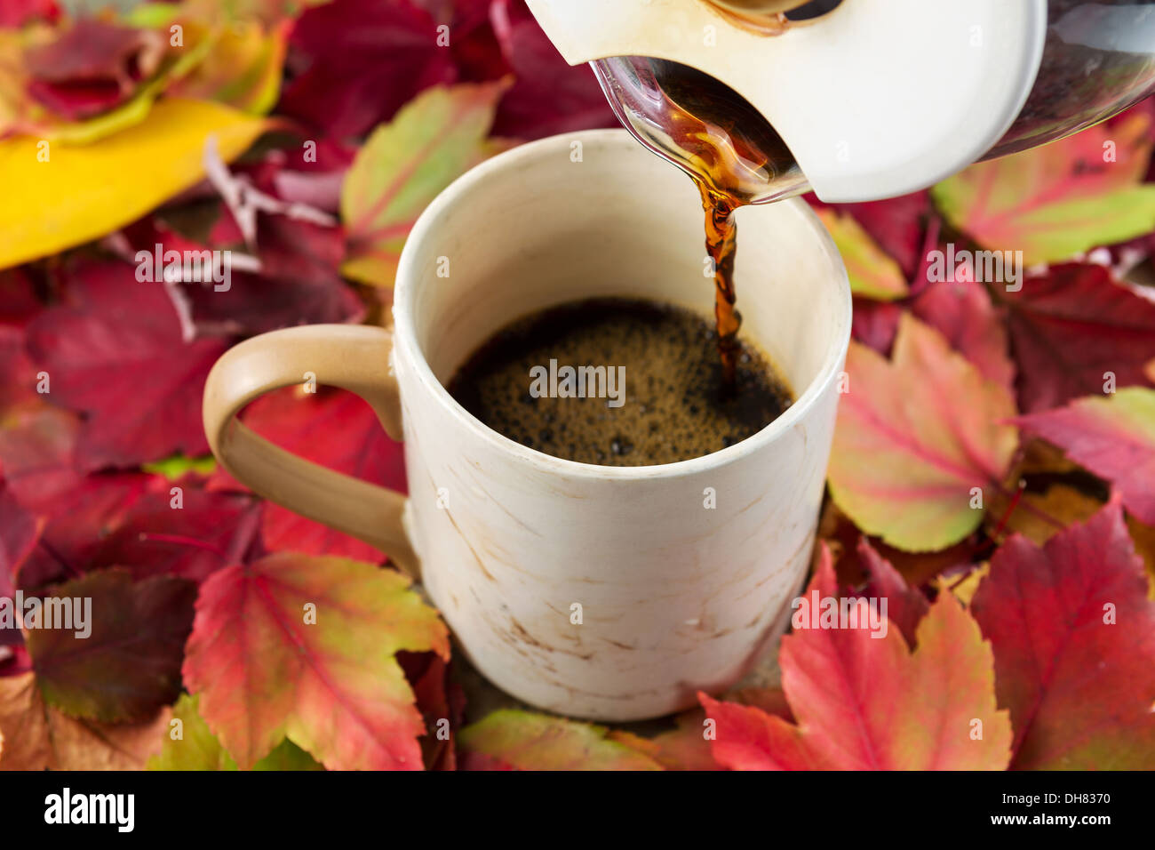 La foto in orizzontale del caffè fresco che viene versato, focus sul beccuccio del vaso, nella tazza stagionali con foglie di autunno che circonda mug Foto Stock