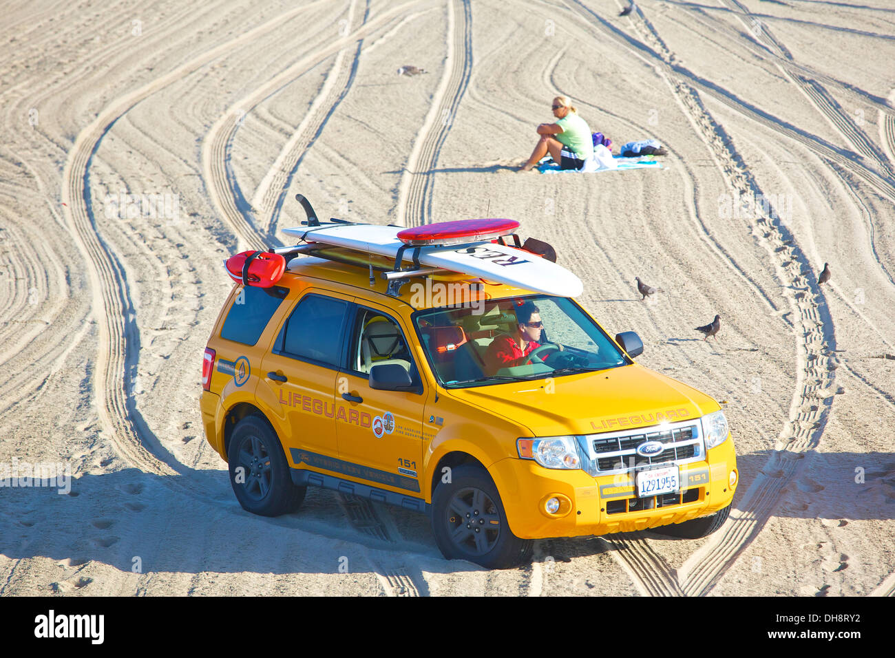 Bagnino di salvataggio nel suo SUV passato alla guida di una donna seduta da sola sulla spiaggia. Foto Stock
