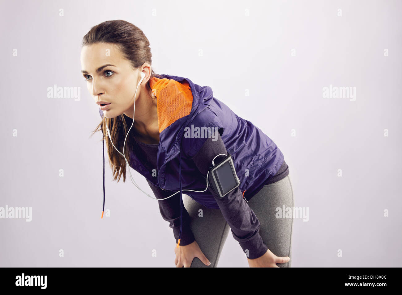 Stanco caucasian atleta femminile sporgendoti dopo il jogging. Giovane donna in abbigliamento sportivo rilassante dopo una corsa su sfondo grigio Foto Stock