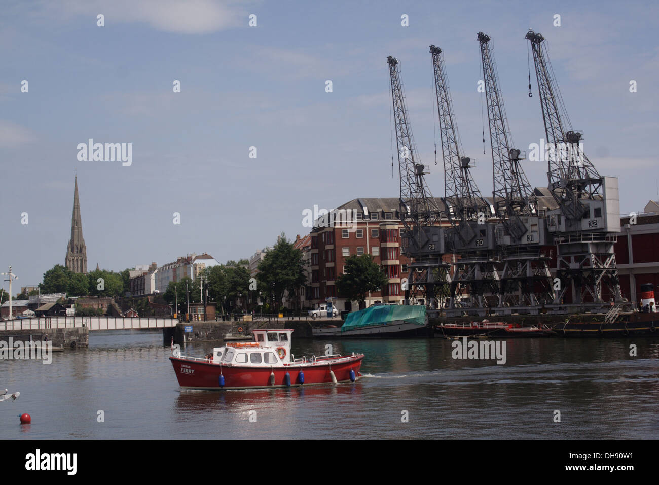 Quattro gru accanto a Bristol City docks con una piccola barca che attraversa il porto Foto Stock