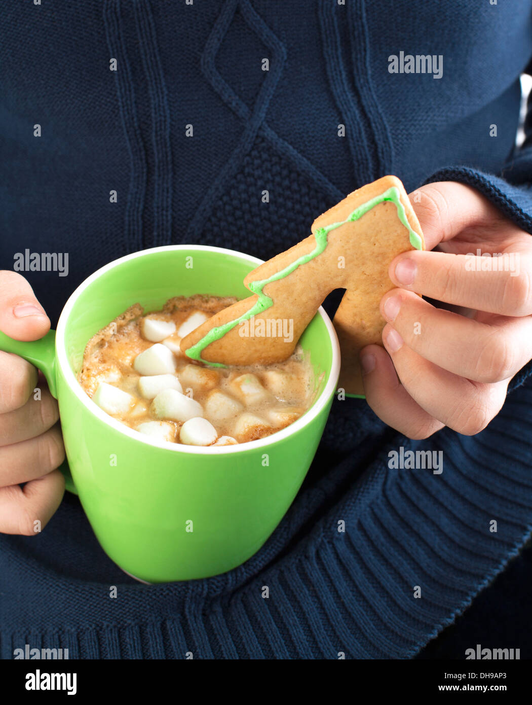 Un primo piano di un ragazzo di immersione di un cookie di zucchero nel cioccolato caldo con marshmallow Foto Stock