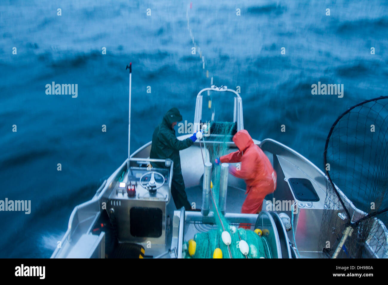 Un salmone commerciale pescatore e il suo marinaio tirando il loro Net a bordo nel brutto tempo sul fiume di rame Appartamenti Foto Stock