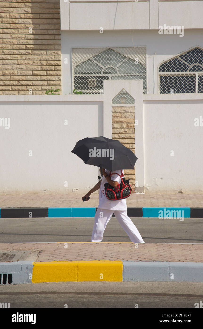Donna si nasconde da estrema Middle Eastern calore sotto il suo ombrello in citta' di Abu Dhabi Foto Stock