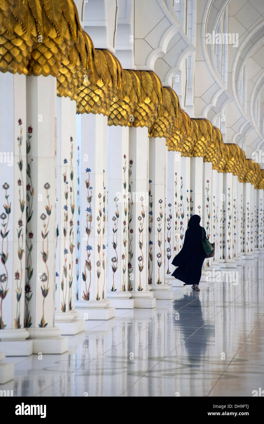 Lone donna cammina attraverso i pilastri della Sheikh Zayed Grande moschea Foto Stock