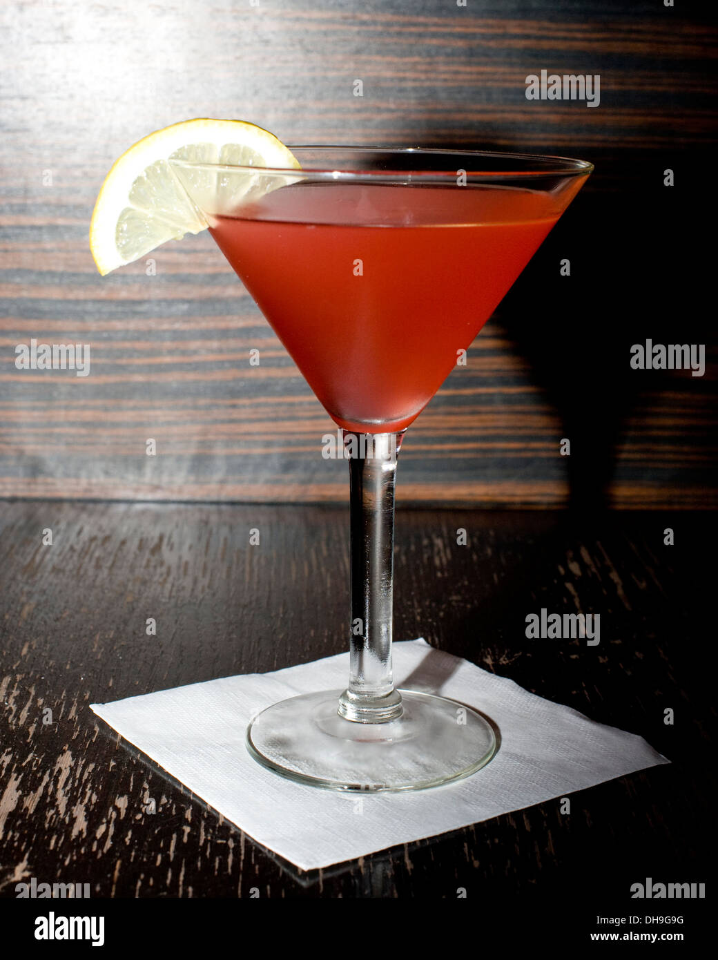 Red il cocktail in una coppetta Martini con un limone guarnire su uno sfondo di legno. Foto Stock