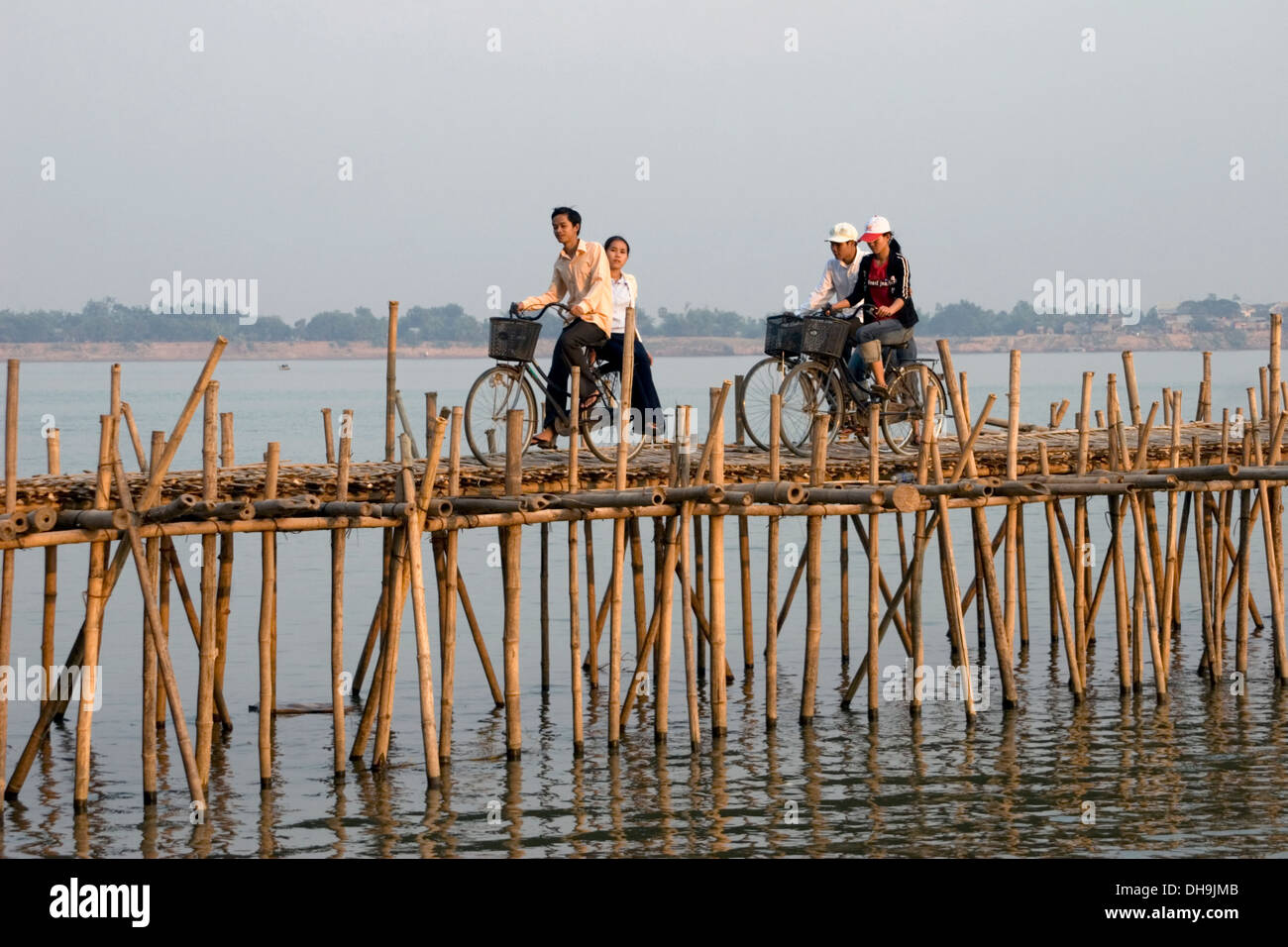 Gli studenti della scuola di equitazione sono le biciclette su un ponte di bambù sul fiume Mekong in Kampong Cham, Cambogia. Foto Stock