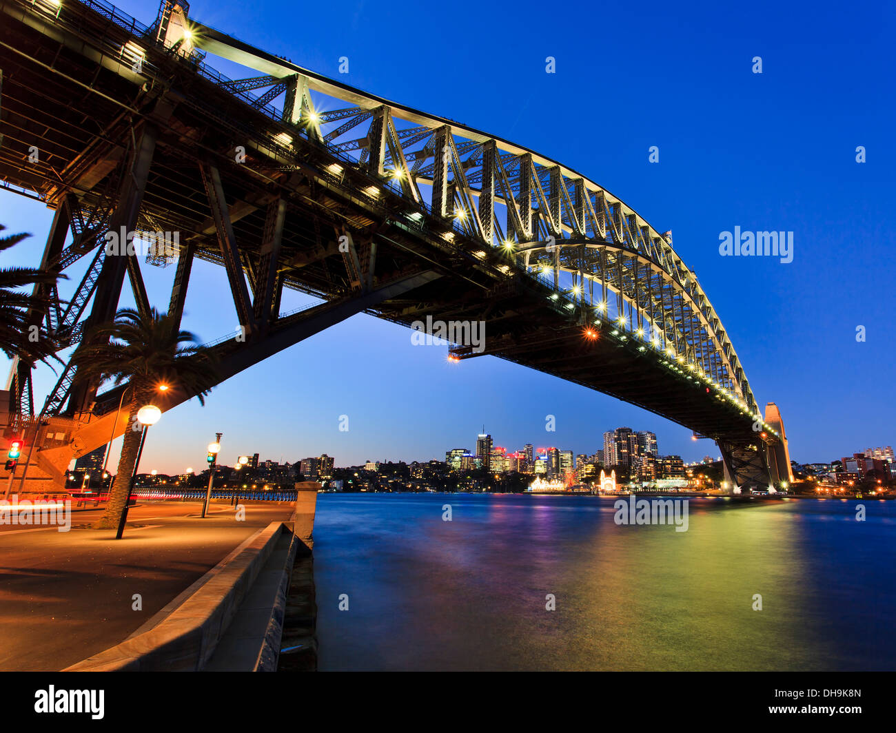 Il Sydney Harbour Bridge vista laterale di arco illuminato con luci riflesso in acqua del porto al tramonto Foto Stock