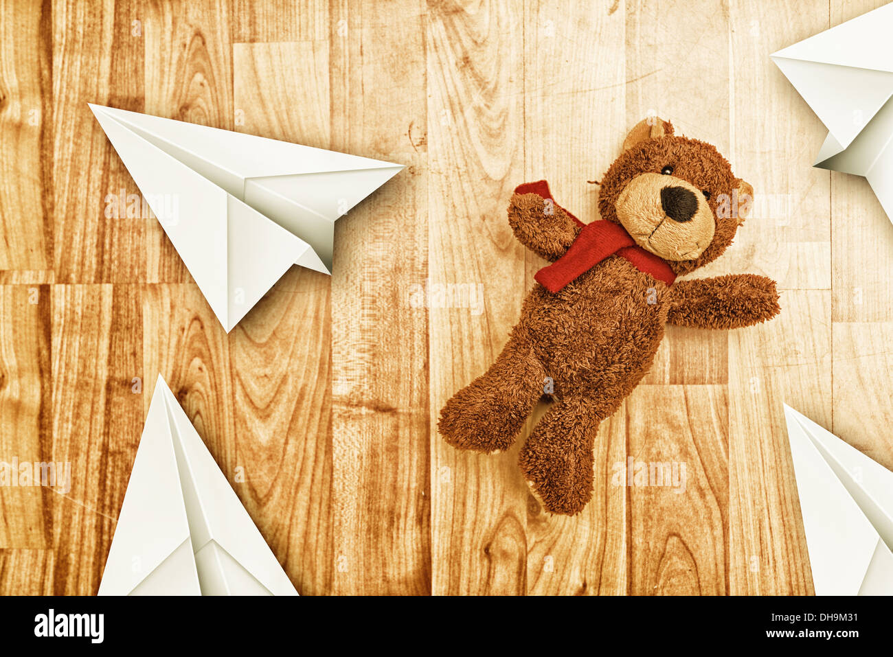 Simpatico orso giocattolo sul laminato pavimento in legno con la carta origami aerei Foto Stock