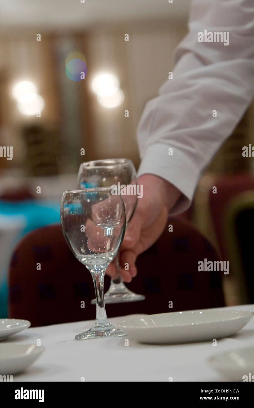 Un cameriere luoghi bicchieri di vino su un tavolo in preparazione per il pasto in un ristorante Foto Stock