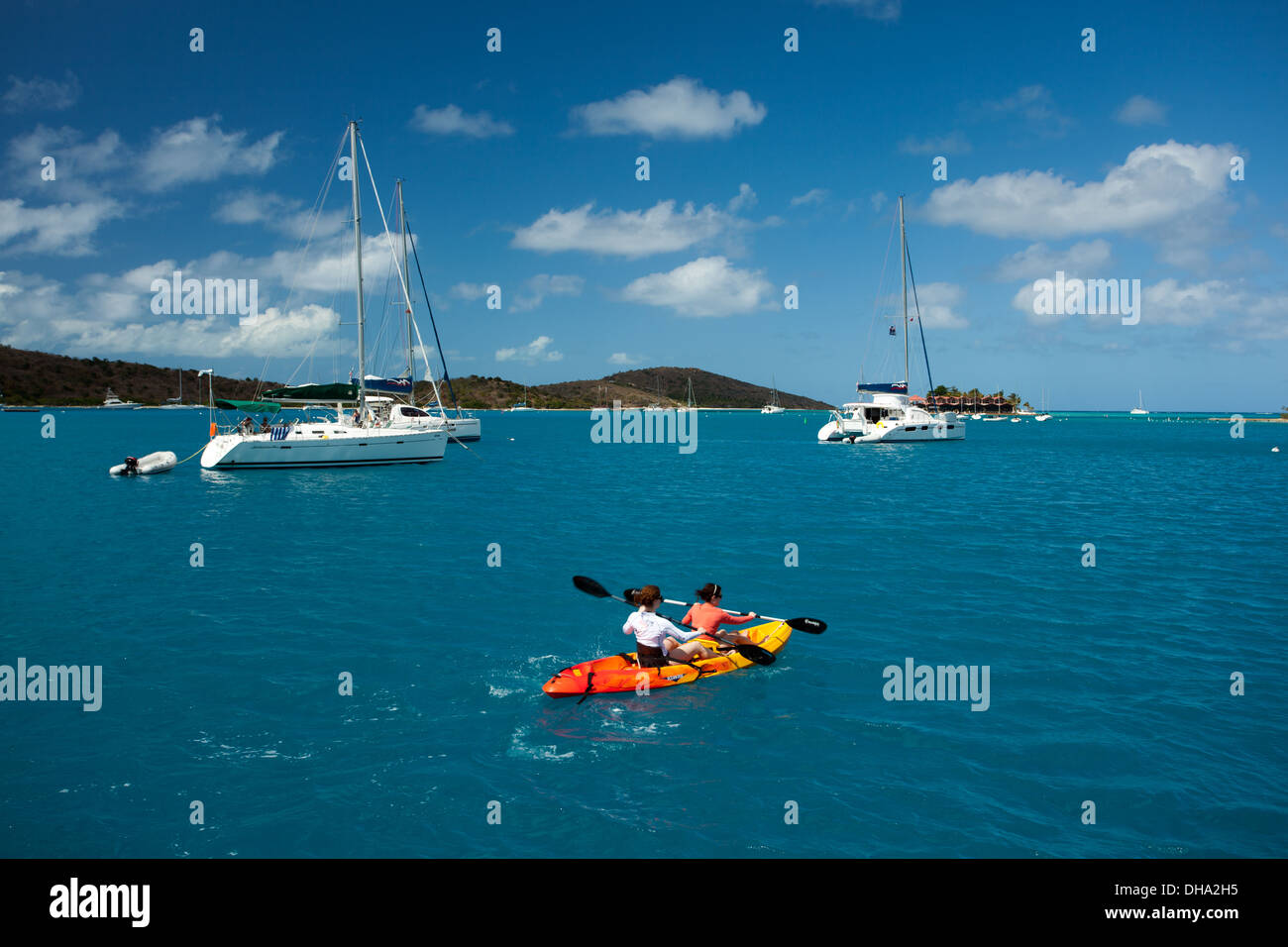 Due persone paddle passato grandi barche a vela bianca nel Mar dei Caraibi nelle Isole Vergini Britanniche su una frizzante giornata estiva Foto Stock
