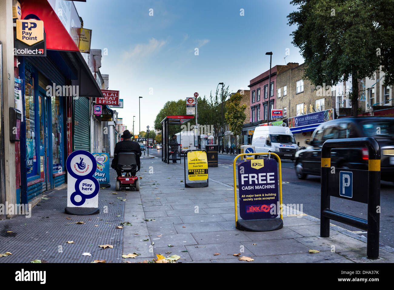 Un uomo su una mobilità scooter passa un'edicola di giornali in Caledonian Road nel quartiere di Islington, Londra Nord. Foto Stock