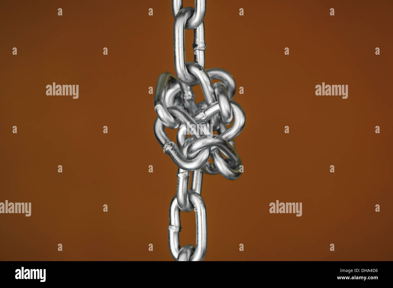 Una catena legati in un nodo contro un sfondo marrone Foto Stock