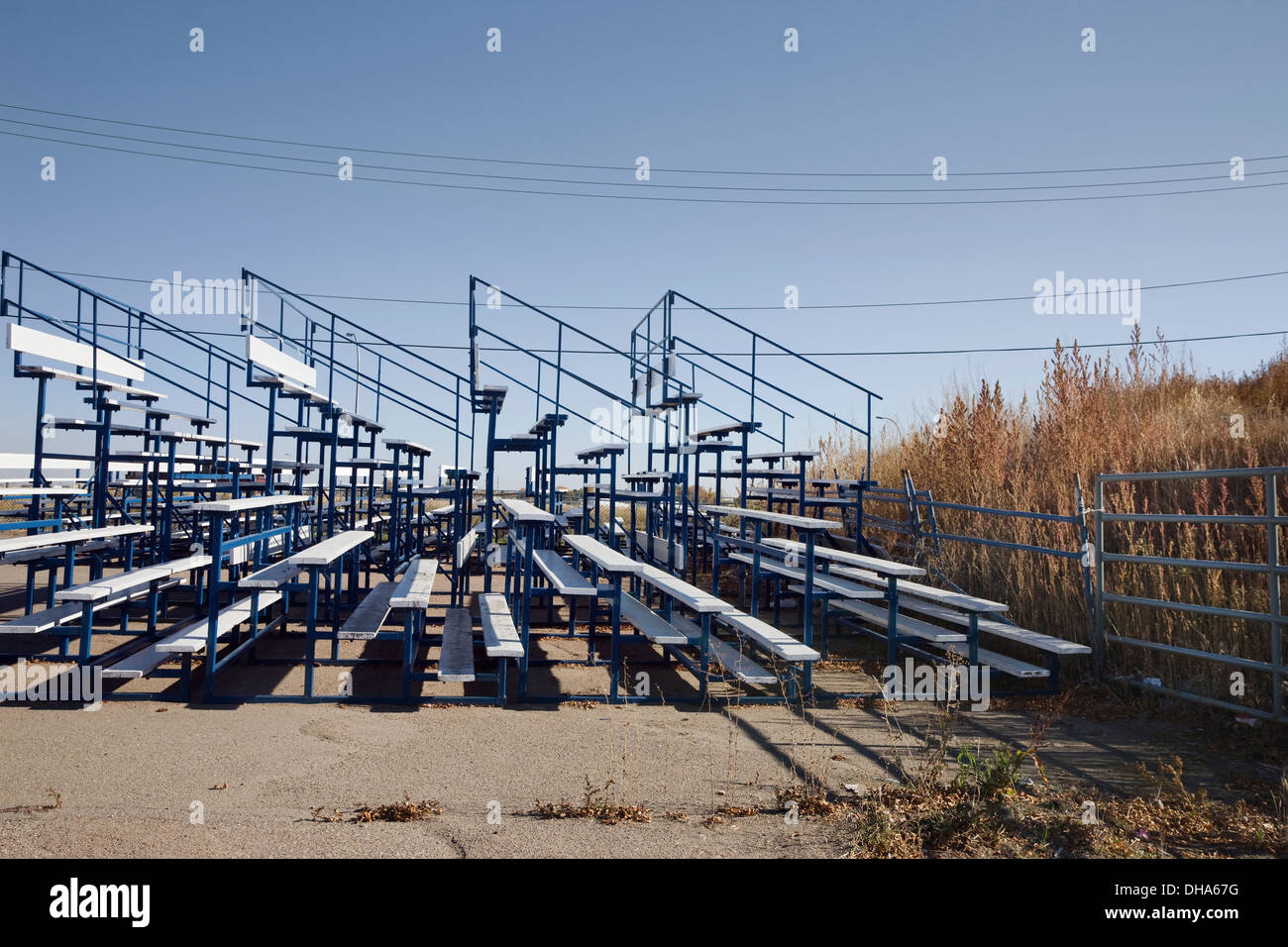 Svuotare Outdoor Stadium Bleachers contro una recinzione che si affaccia su di un campo di alte erbe: Lethbridge, Alberta, Canada Foto Stock