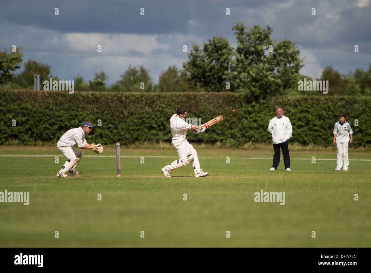 Village cricket. Il battitore tira piazza la palla del paletto con il wicketkeeper in attesa di balzare mentre un fielder e un Foto Stock