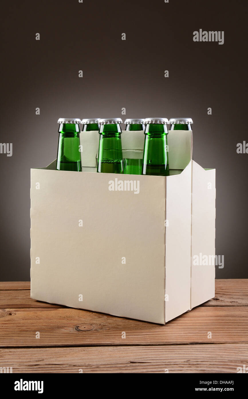 Primo piano di un six pack di verde bottiglie di birra su una tavola in legno rustico. Formato verticale con una luce di colore grigio scuro dello sfondo spot. Foto Stock