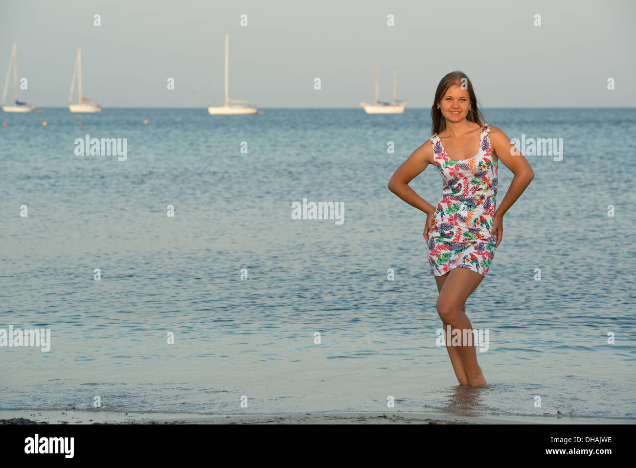 Giovane donna bionda di fronte di mare e yacht, indossando abiti colorati Foto Stock