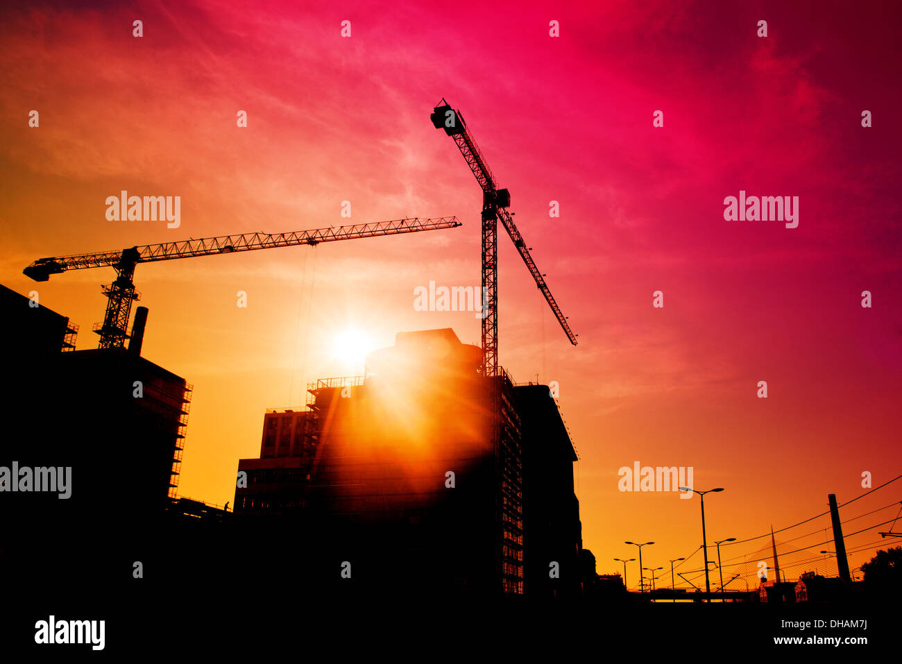 Sito in costruzione nel tramonto, sagome di gru edili contro la luce del sole. Foto Stock