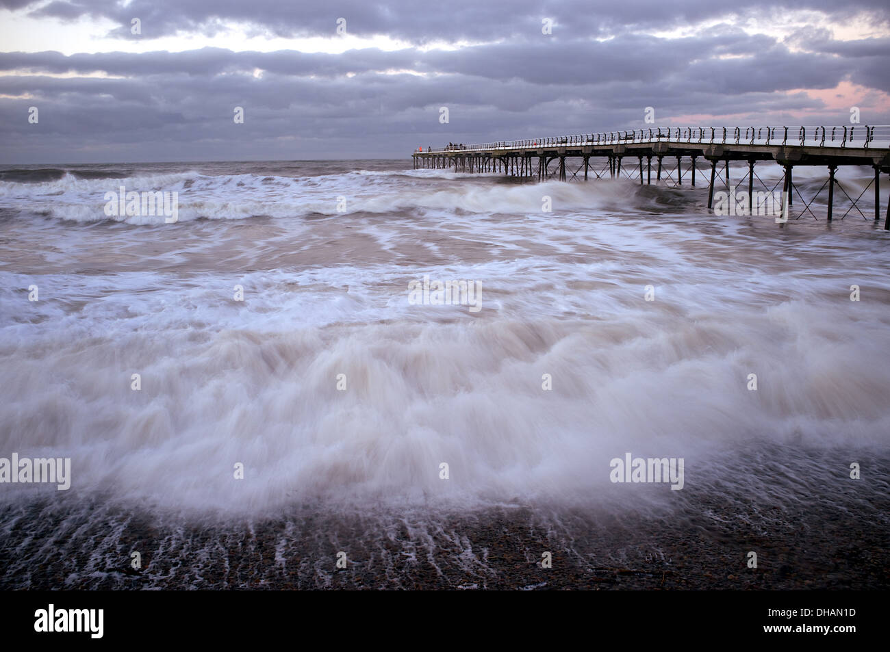 Il mare si precipita a riva su un giorno di tempesta e volute intorno a un lungo molo a destra del telaio. Foto Stock