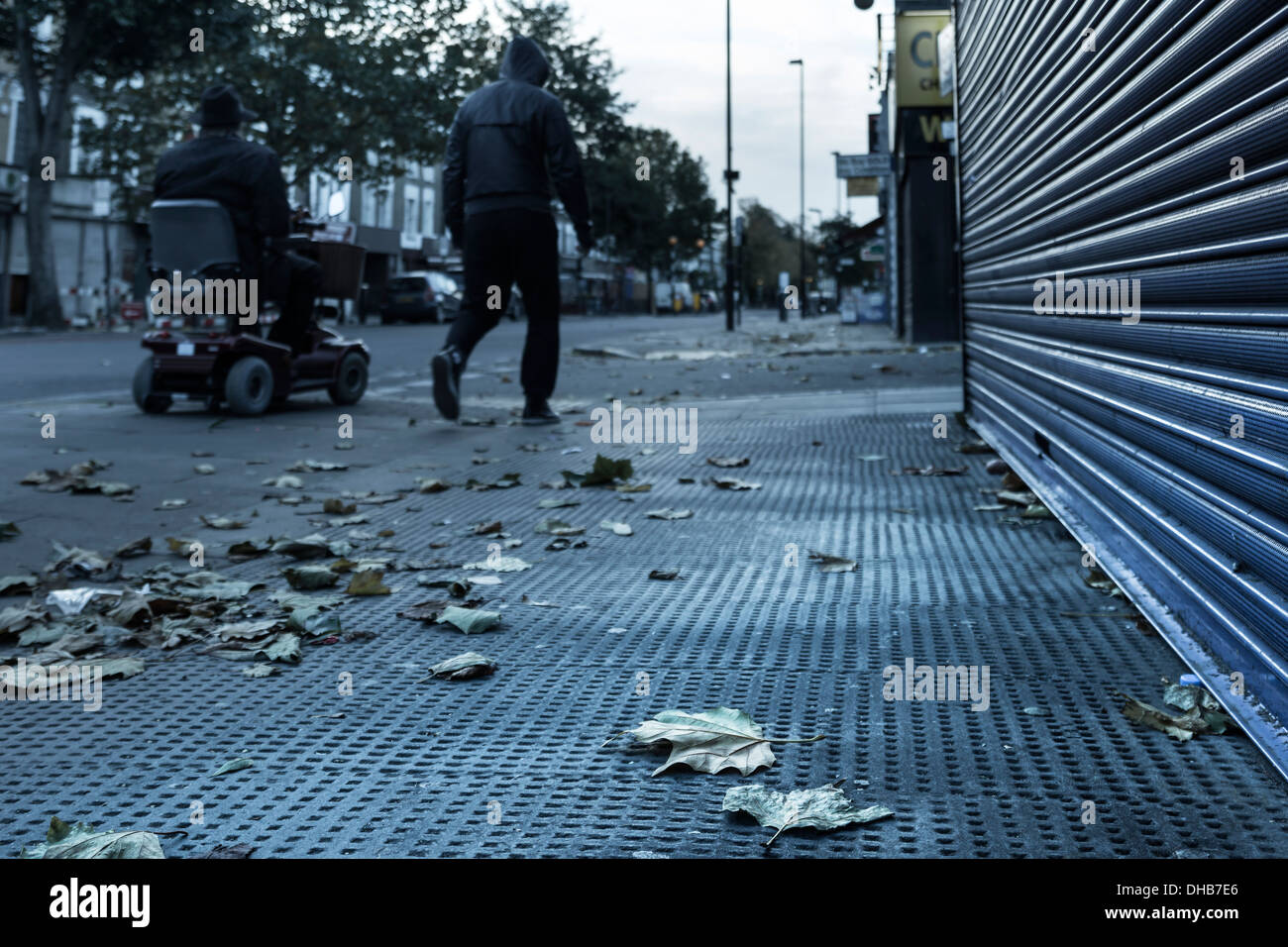 Una gioventù passa un uomo su uno scooter di mobilità lungo il Caledonian Road nel quartiere di Islington, Londra del nord su una mattina di novembre. Foto Stock