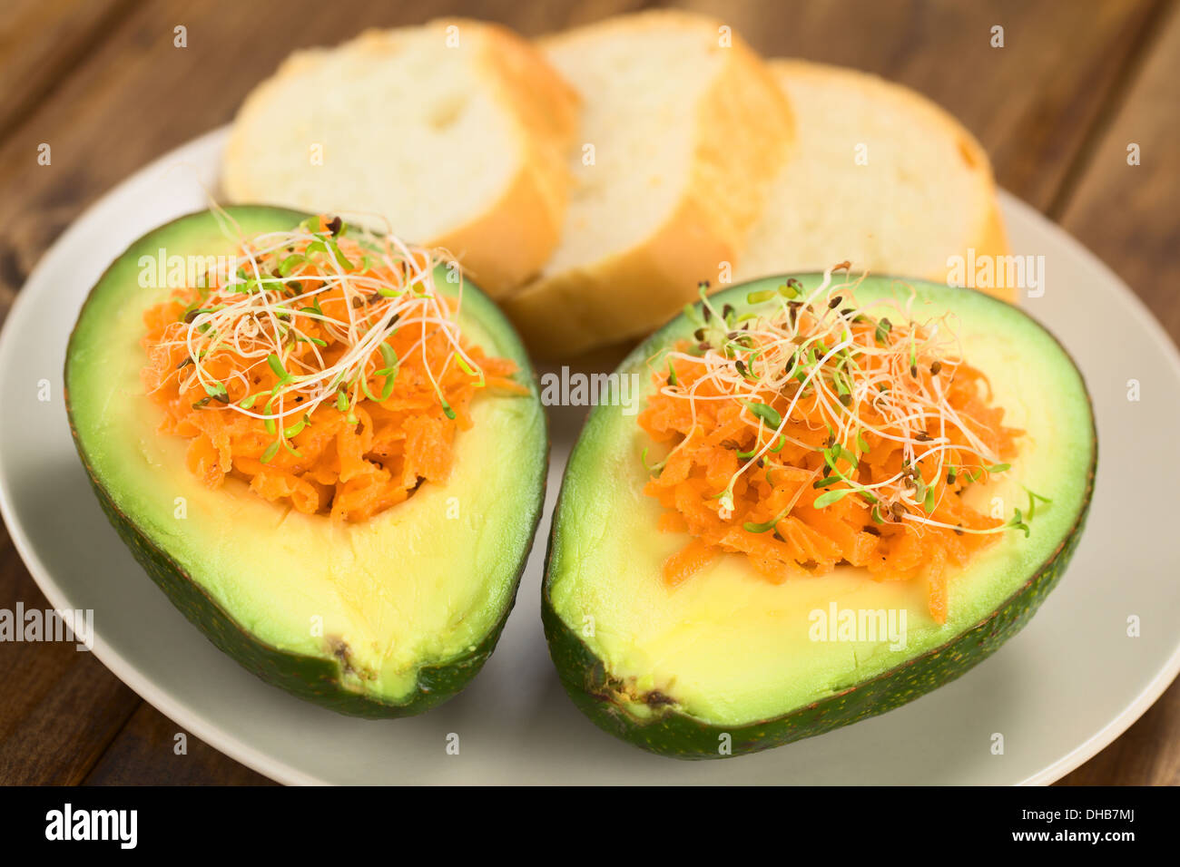 Metà di Avocado riempito con carote grattugiate e cosparso di germogli alfalfa servito sulla piastra con baguette fette Foto Stock