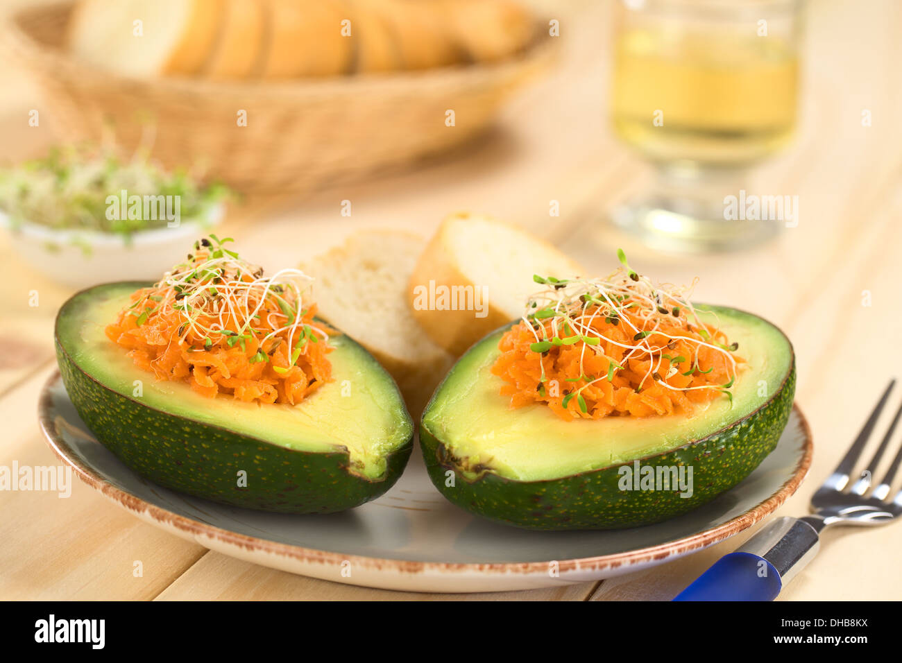 Metà di Avocado riempito con carote grattugiate e cosparso di germogli alfalfa servito sulla piastra con baguette fette Foto Stock