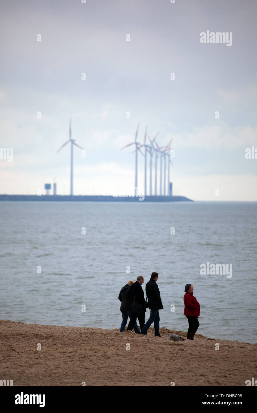 La gente sulla spiaggia di Knokke, Fiandre, in Belgio, con le turbine eoliche del parco eolico di Zeebrugge dietro. Foto Stock