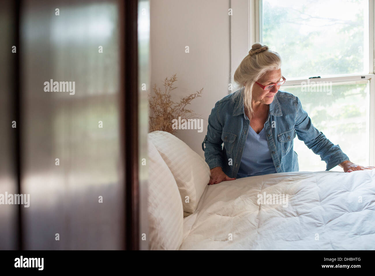 Un casale di campagna, una donna che compongono un letto in una camera da letto. Foto Stock