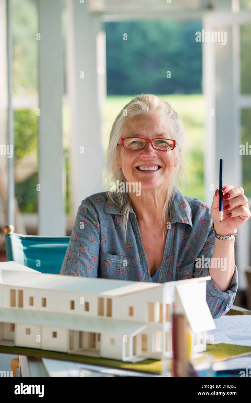 Un agriturismo cucina. Un modello di una casa sul tavolo. La progettazione di una casa. Una donna seduta in possesso di una penna. Foto Stock