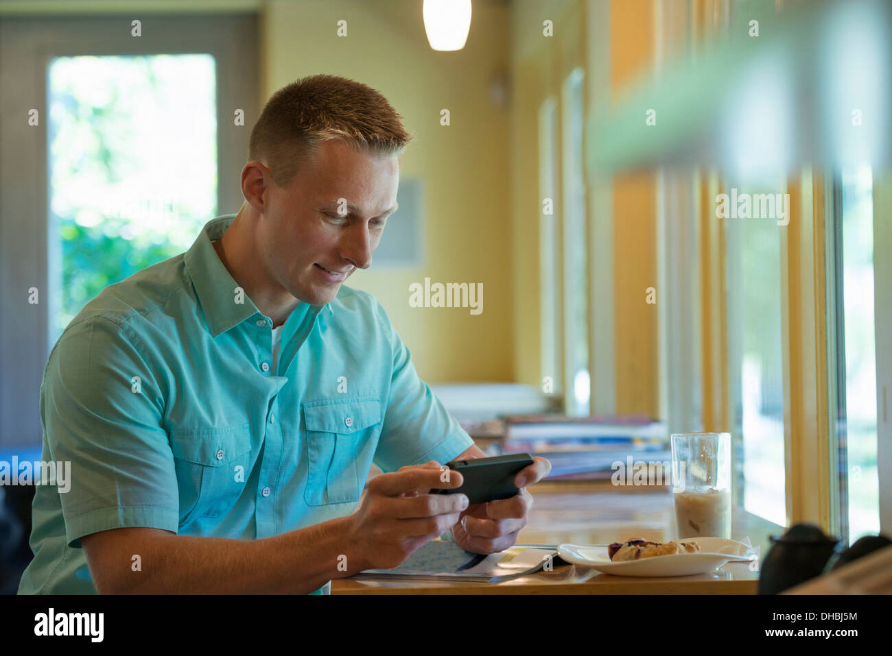 Un uomo con corti capelli ritagliata seduti ad un tavolo del bar, utilizzando un telefono intelligente. Foto Stock