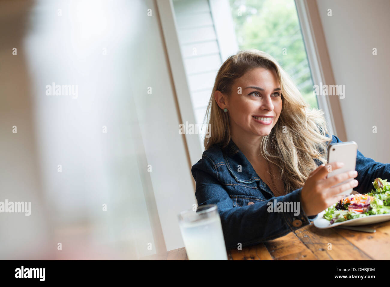 Una giovane donna che utilizza una smart phone, seduti ad un tavolo. Caffè e un panino. Foto Stock