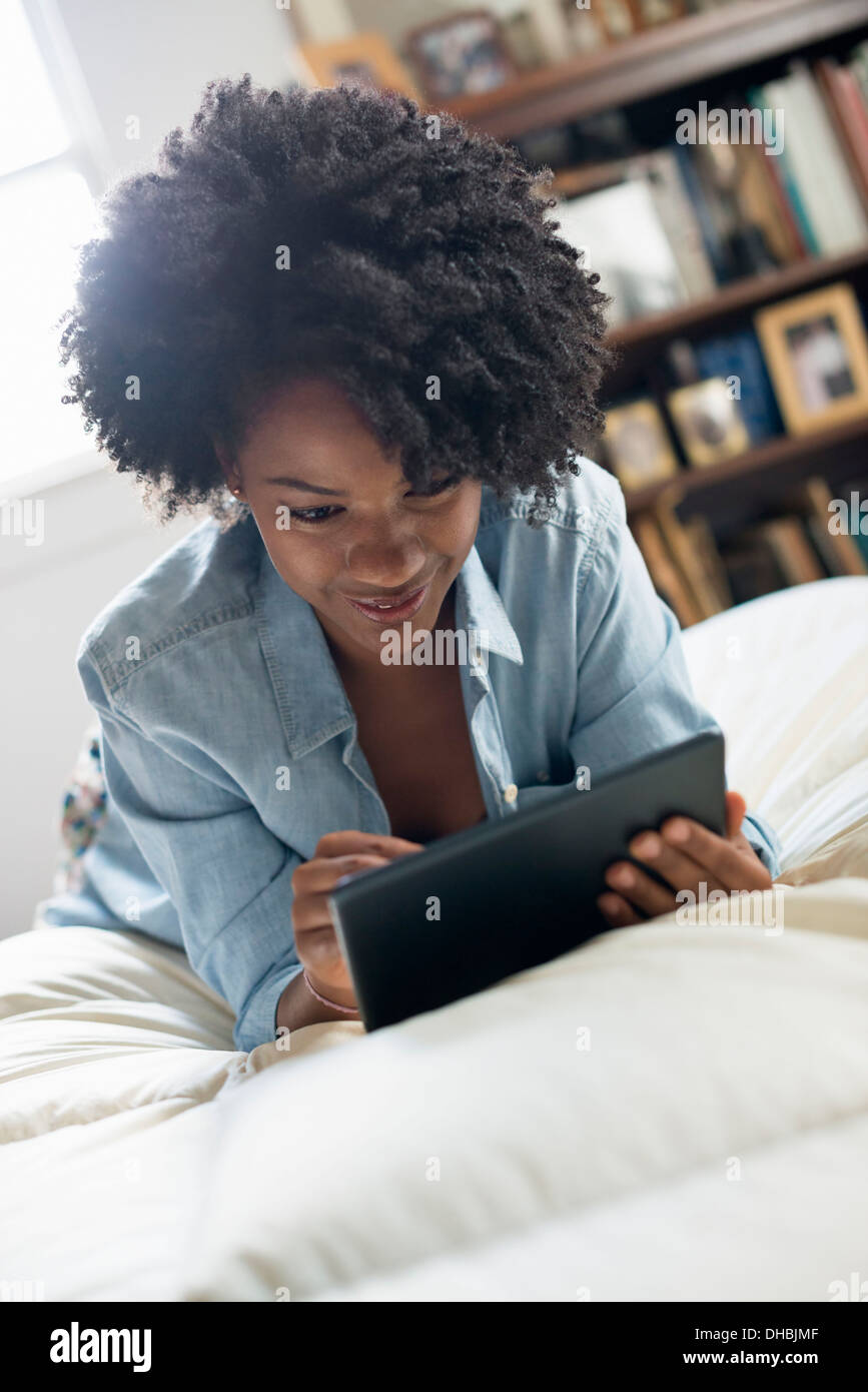 Una donna sdraiata su un letto, utilizzando una tavoletta digitale. Foto Stock