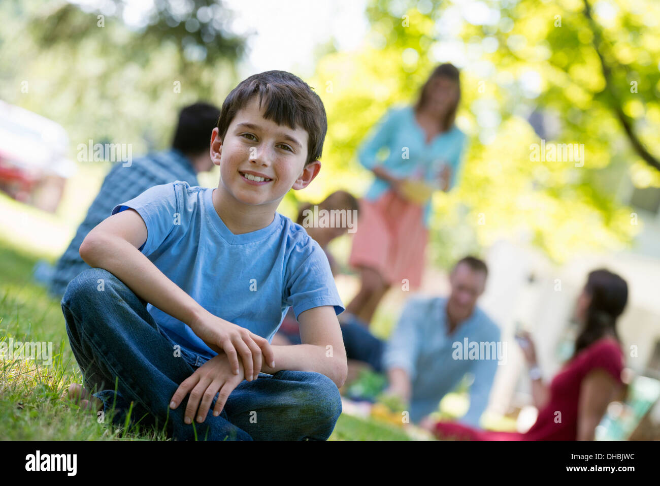 Un gruppo di adulti e bambini seduti sul prato sotto l'ombra di un albero. Una festa di famiglia. Foto Stock