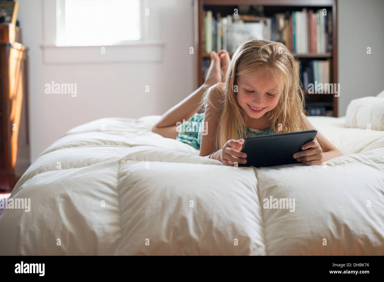 Una giovane ragazza seduta sul suo letto utilizzando una tavoletta digitale. Foto Stock