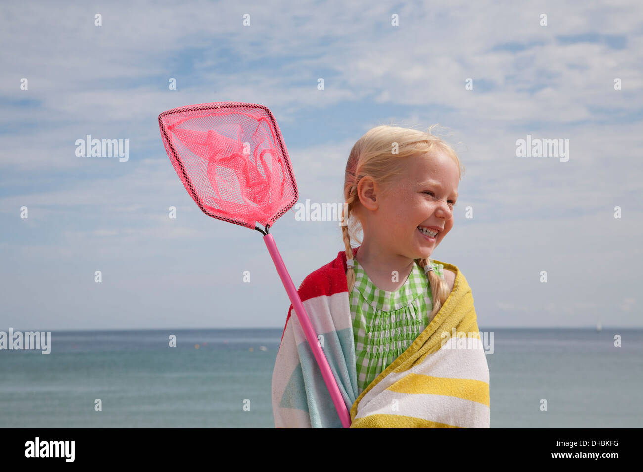 Una giovane ragazza con un telo da spiaggia intorno a lei le spalle, il trasporto di una piccola rete da pesca. Foto Stock