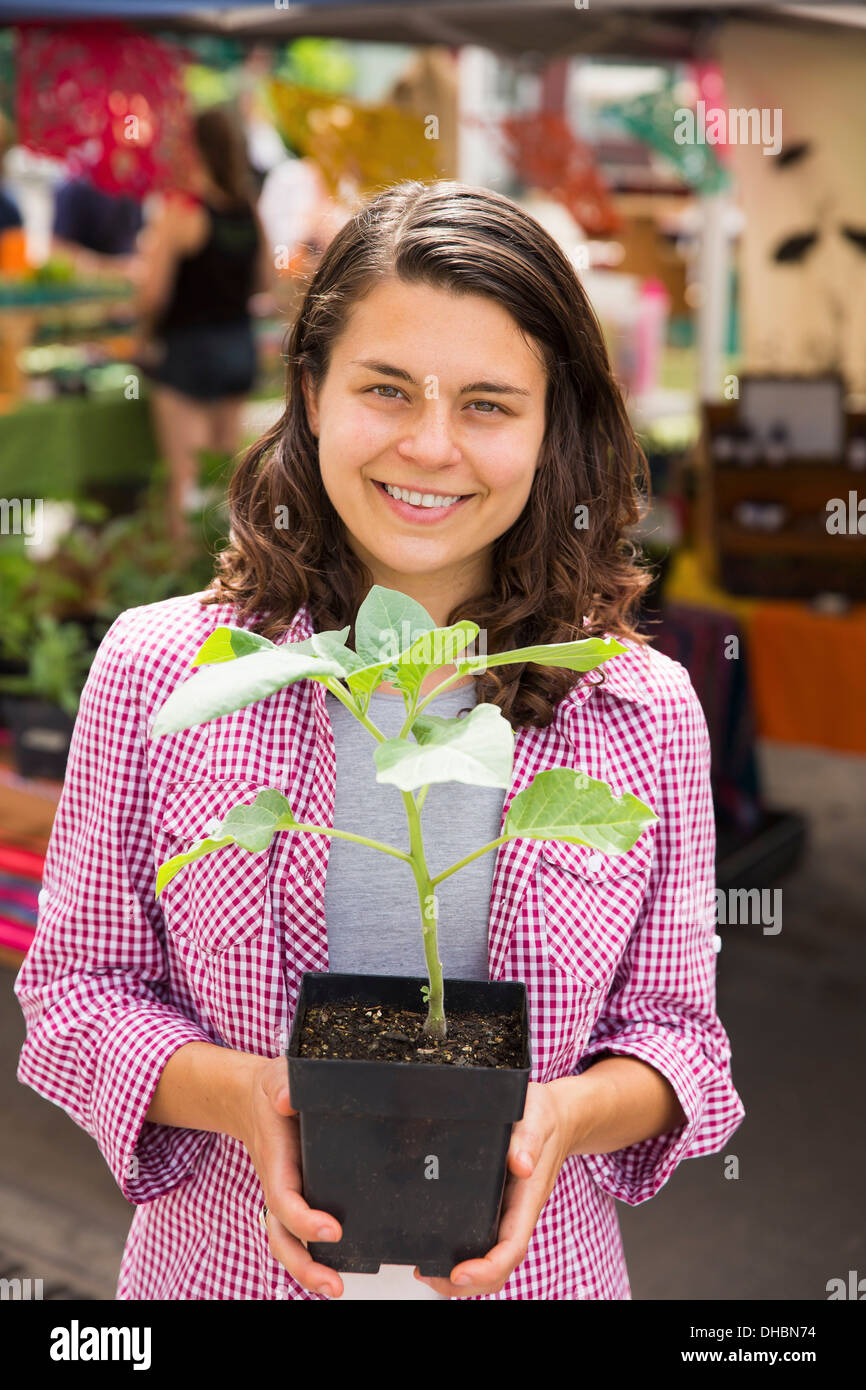 Una giovane donna che tiene una piccola pianta in un vaso. Farm stand. Foto Stock