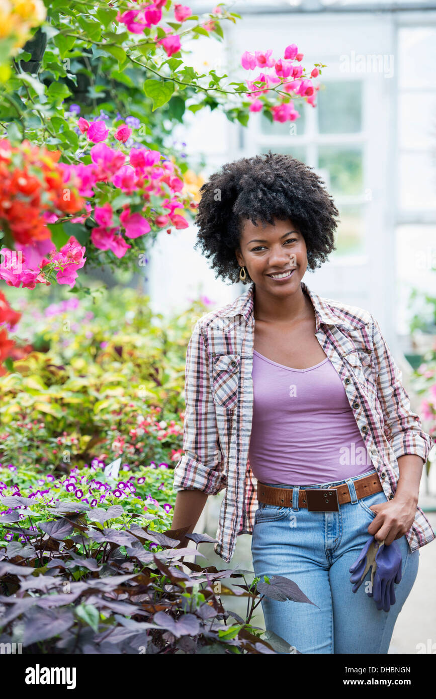 Una donna in un vivaio circondato da piante fiorite e foglie verdi. Foto Stock