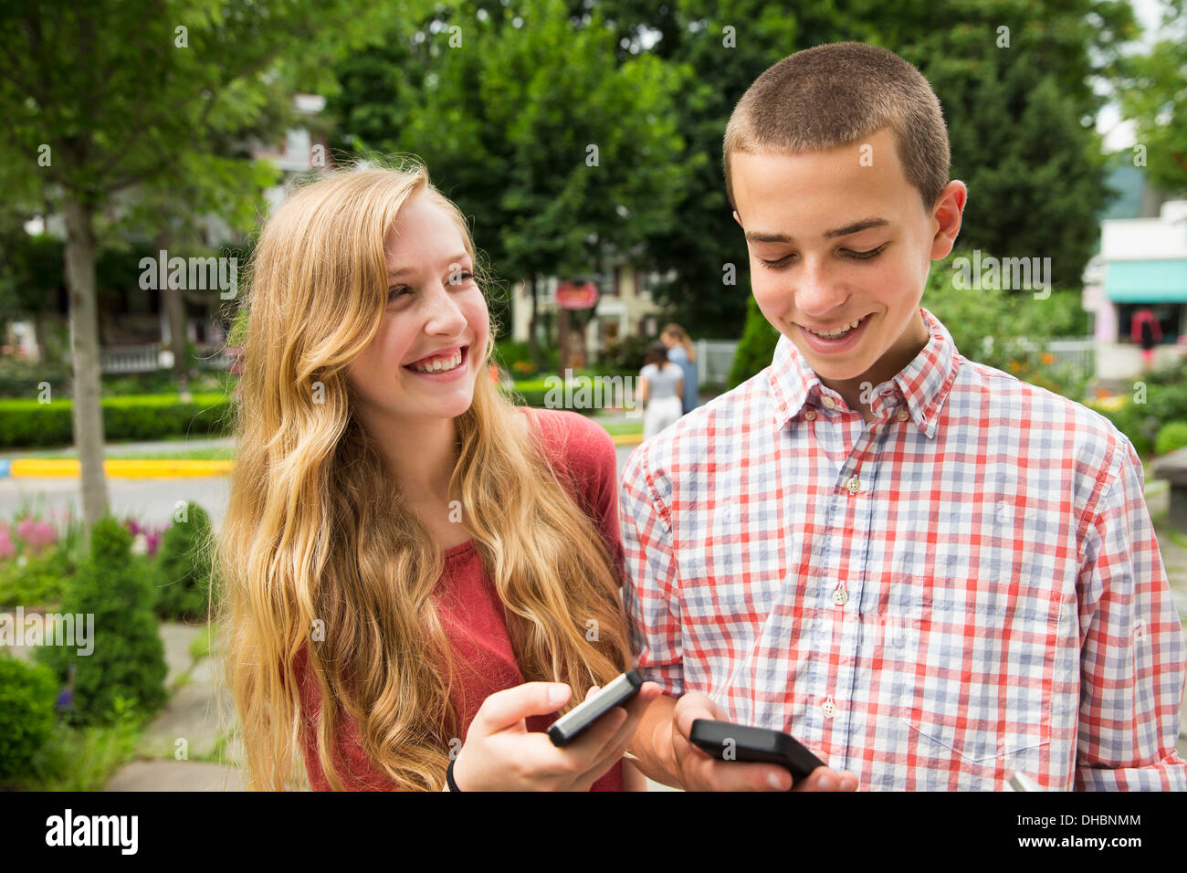 Due amici, un ragazzo e una ragazza guardando i loro telefoni cellulari. Foto Stock