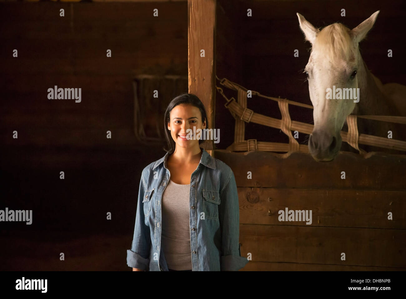 Un agriturismo biologico nelle Catskills Mountains. Una donna in piedi in una stabile, con un cavallo bianco guardando sopra la stalla. Foto Stock