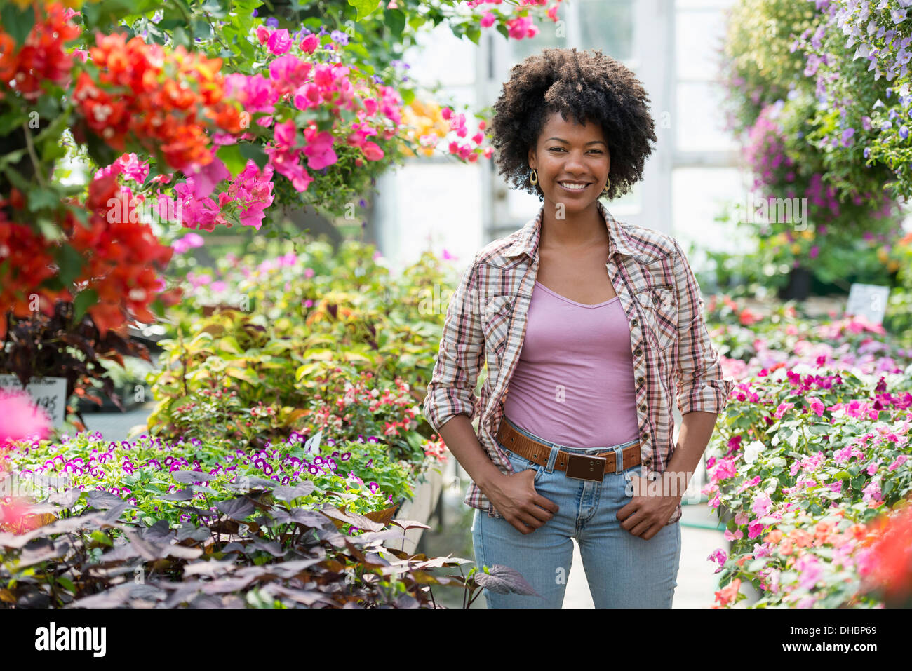 Una donna in un vivaio circondato da piante fiorite e foglie verdi. Foto Stock