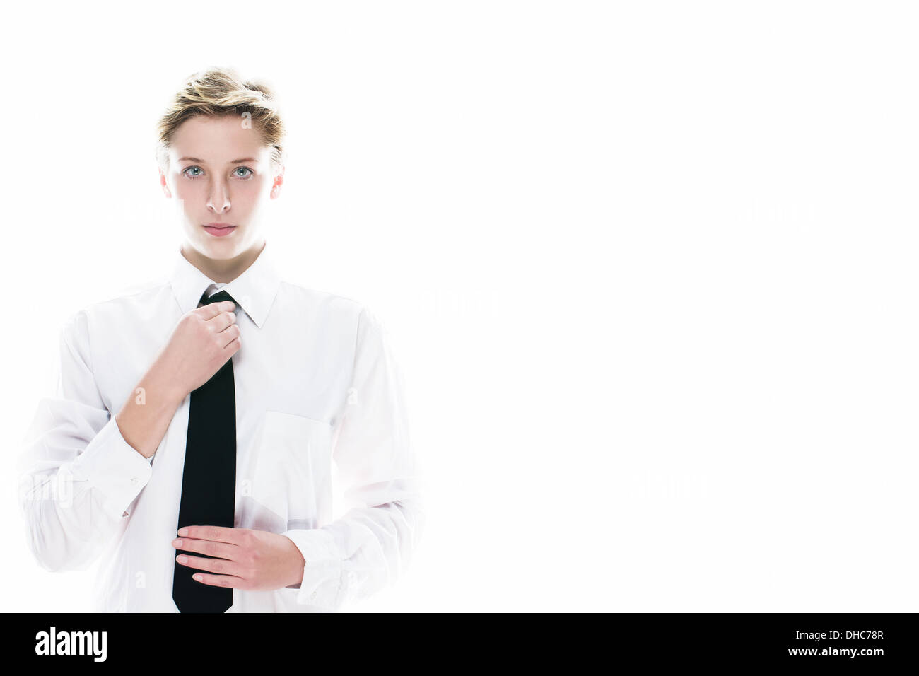 Giovane donna androgino correggendo la sua cravatta nera su sfondo bianco Foto Stock